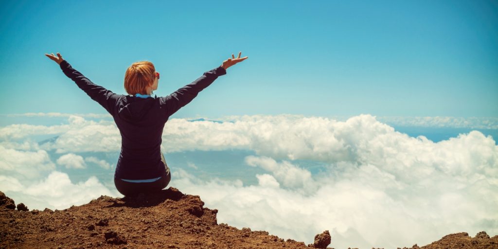 Woman sitting on a cliff with her arms outstretched
