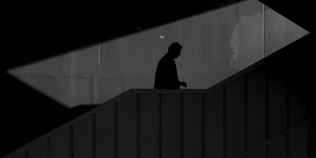 A shadowed figure walking through dim light, reflecting the heightened awareness behind why do I feel like I’m being watched.